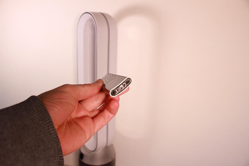 Die kleine und gebogene Fernbedienung vom Dyson Purifier Cool Autoreact TP7A Luftreinigers wird in der Hand gehalten